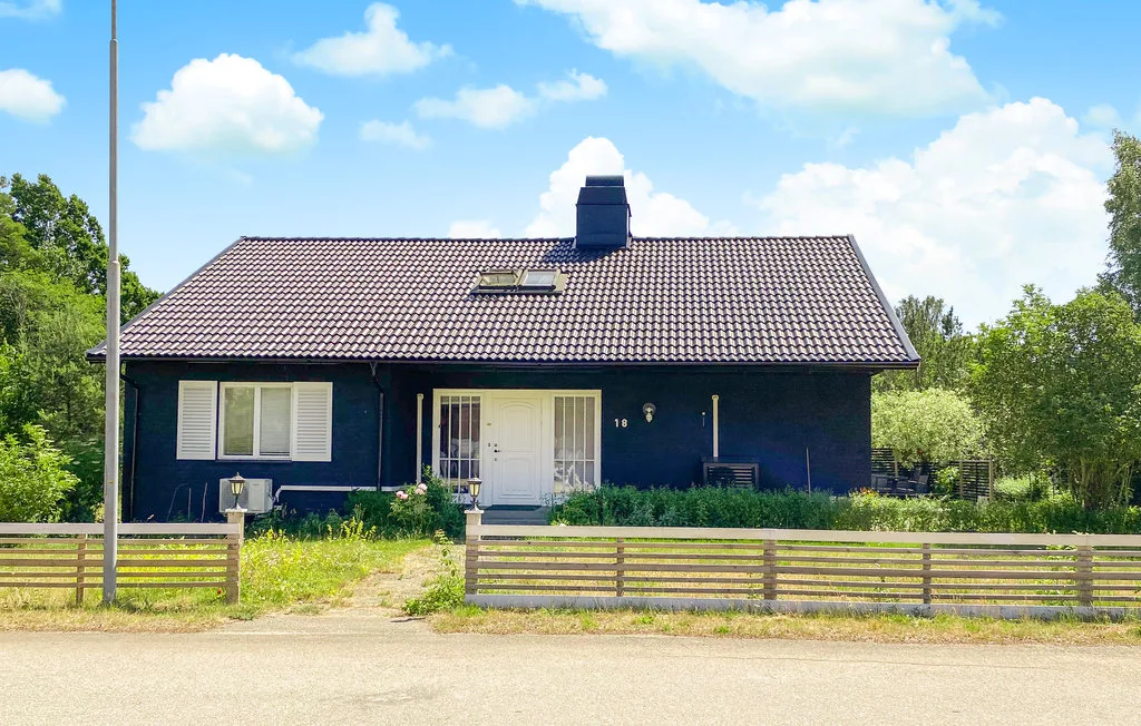 A dark house with a tiled roof stands behind a wooden fence.