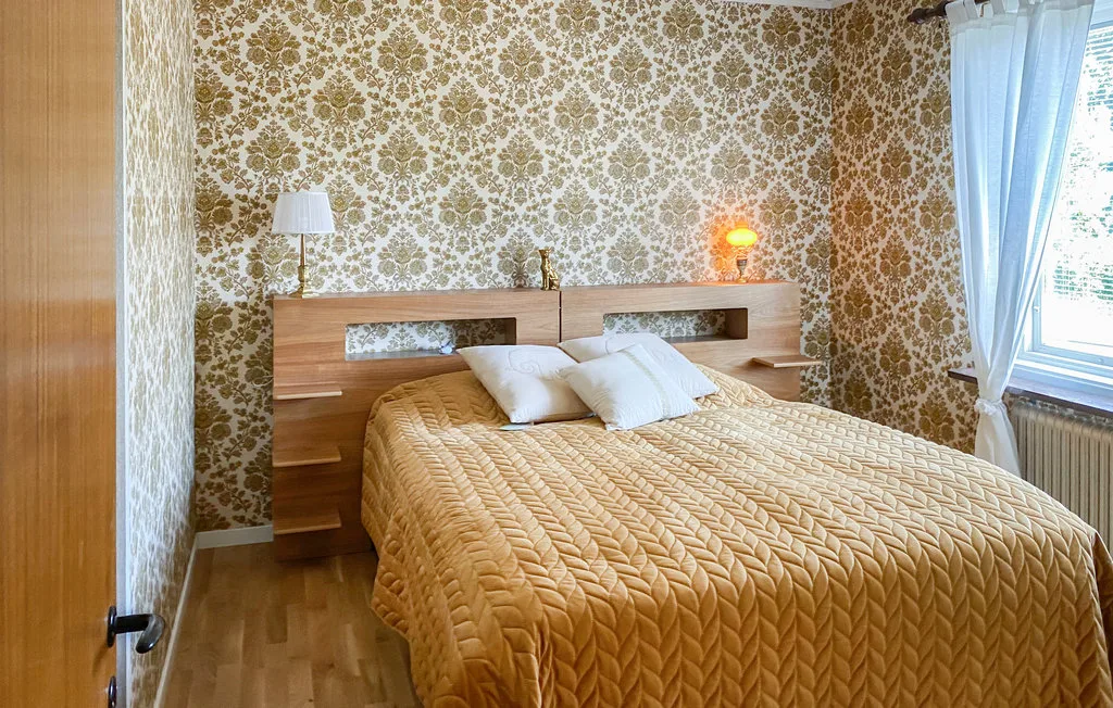 A bedroom with a bed beneath patterned wallpaper and beside a curtained window.