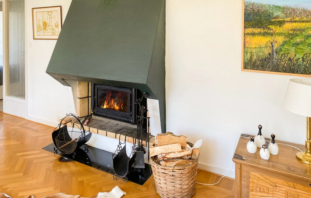 A living room fireplace with a fire burning beside a basket of logs.