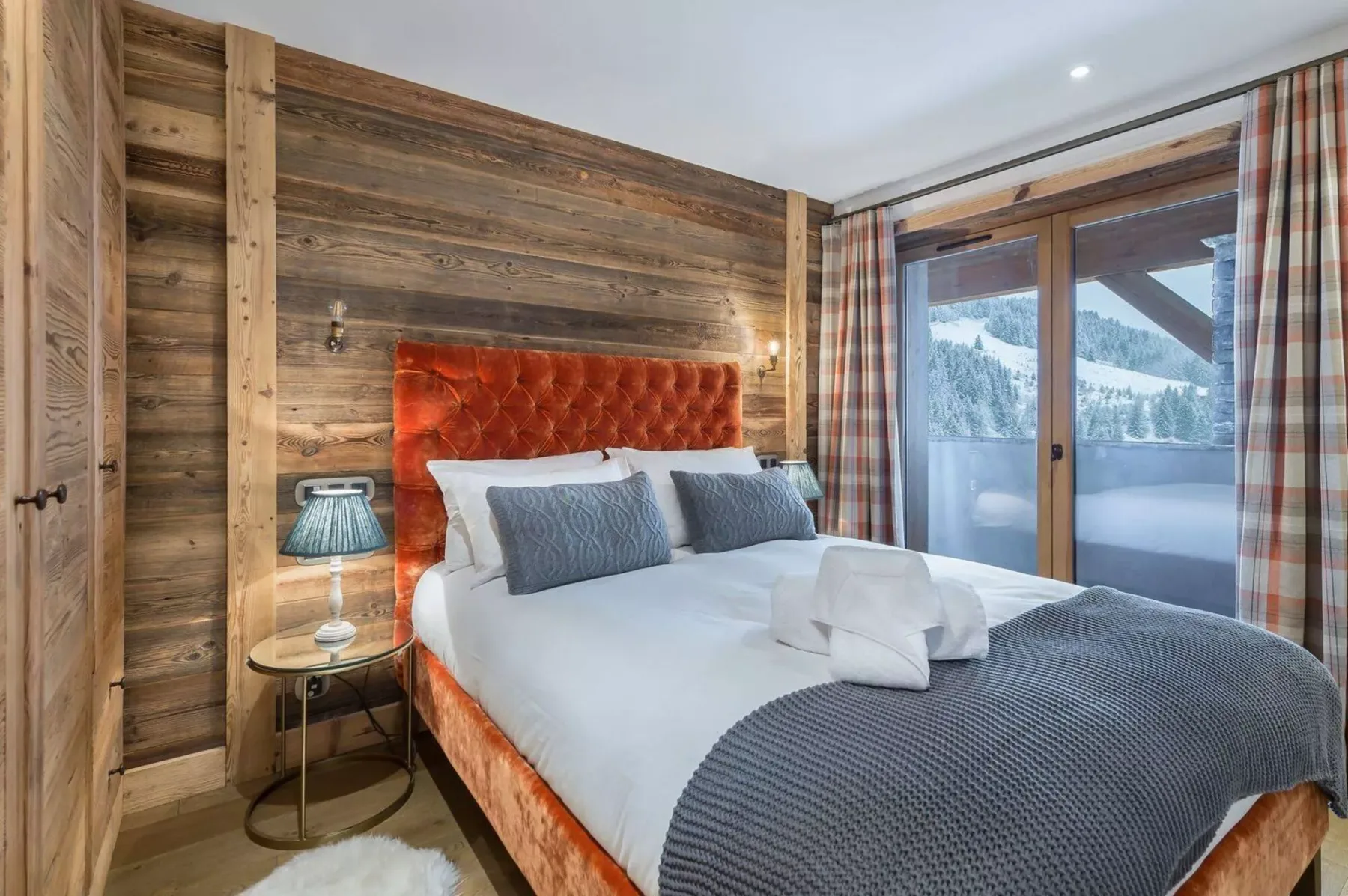 A bedroom with a bed against a wood-paneled wall and glass doors.