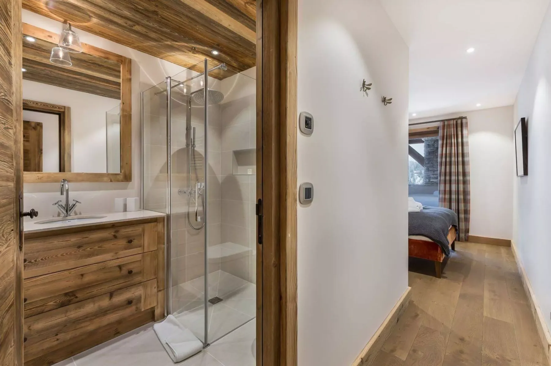 A bathroom with a wood vanity and glass shower beside a bedroom hallway.