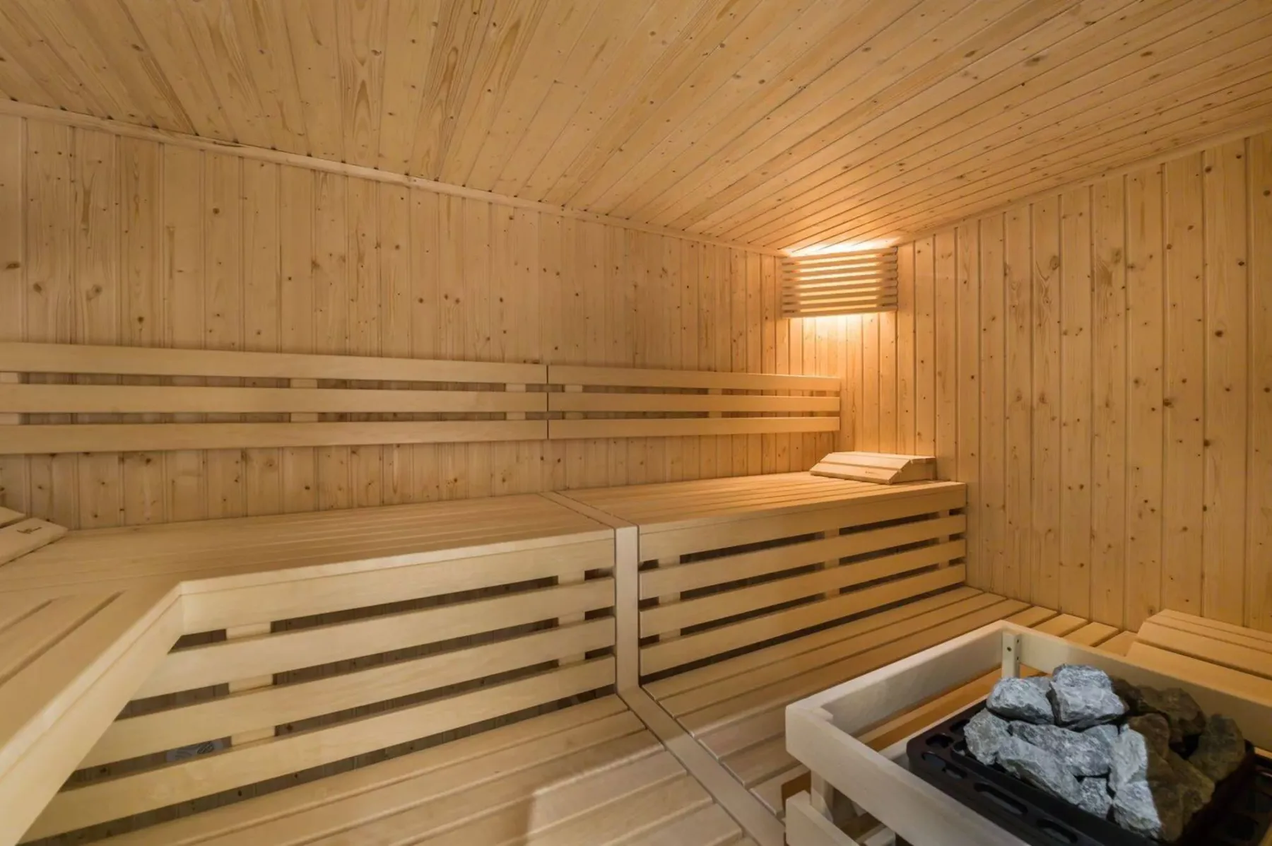 A wood-paneled sauna with tiered seating and a heater filled with stones.