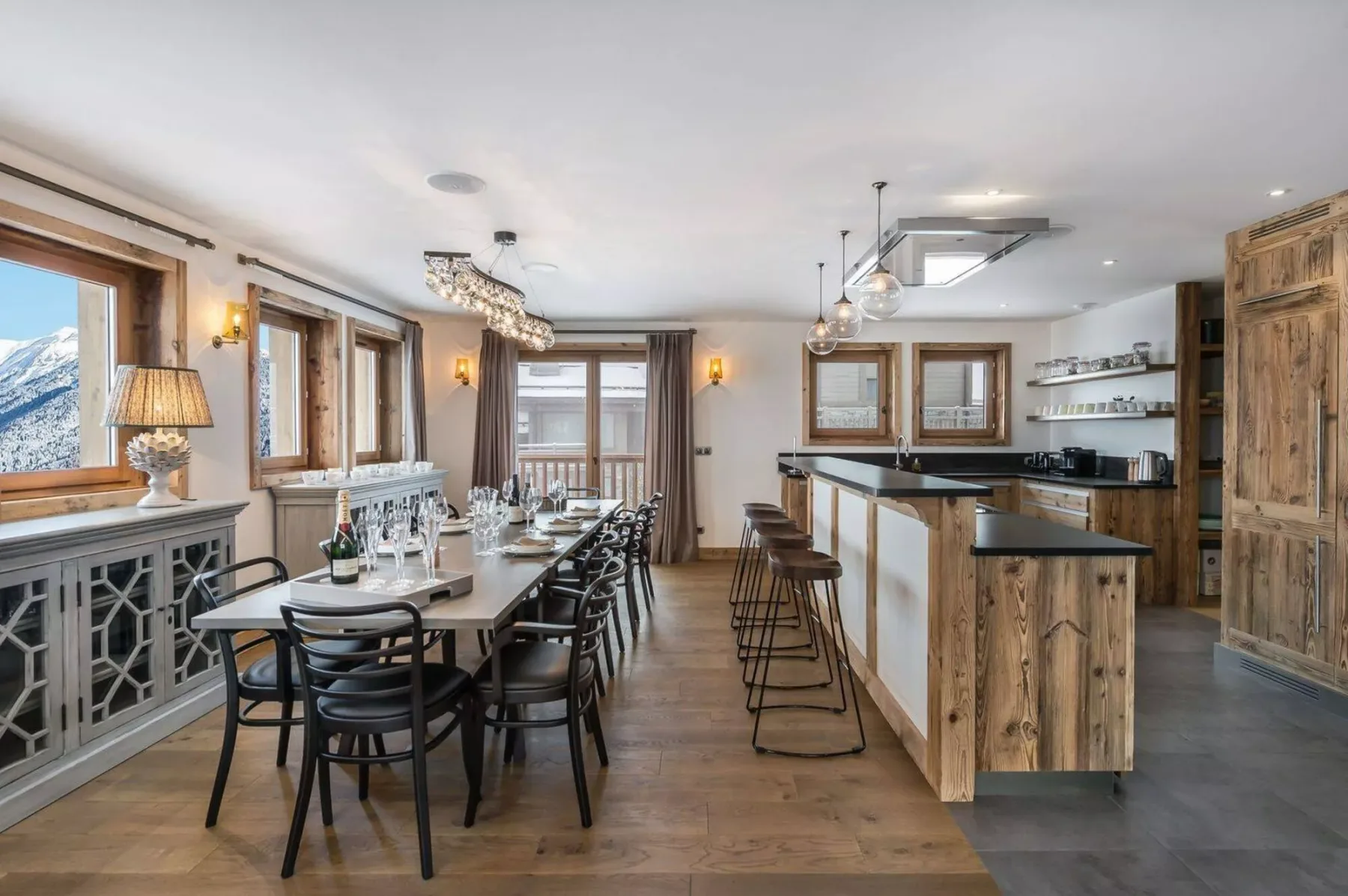 Comedor y cocina con una mesa larga, asientos de barra y gabinetes de madera.