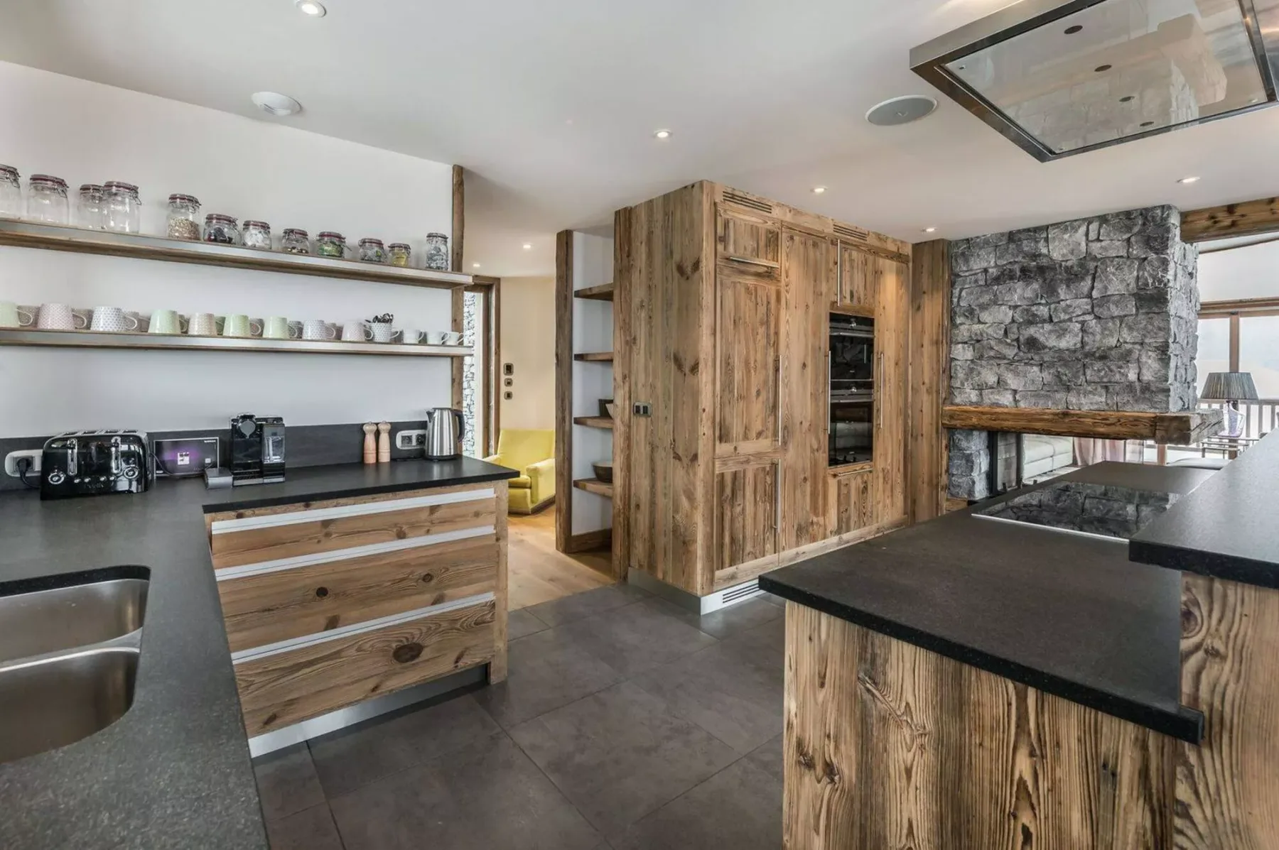 A spacious kitchen with wood cabinetry, dark countertops, and a stone accent wall.