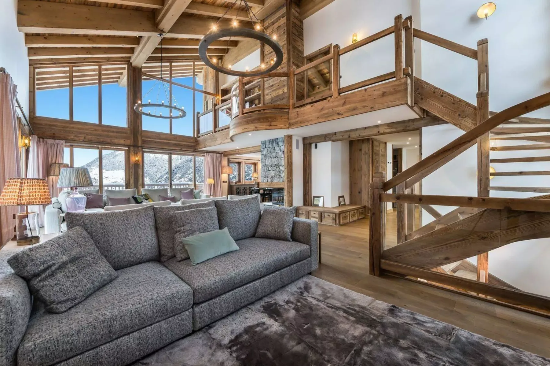 A spacious living room with gray seating beneath a wooden loft and exposed beams.