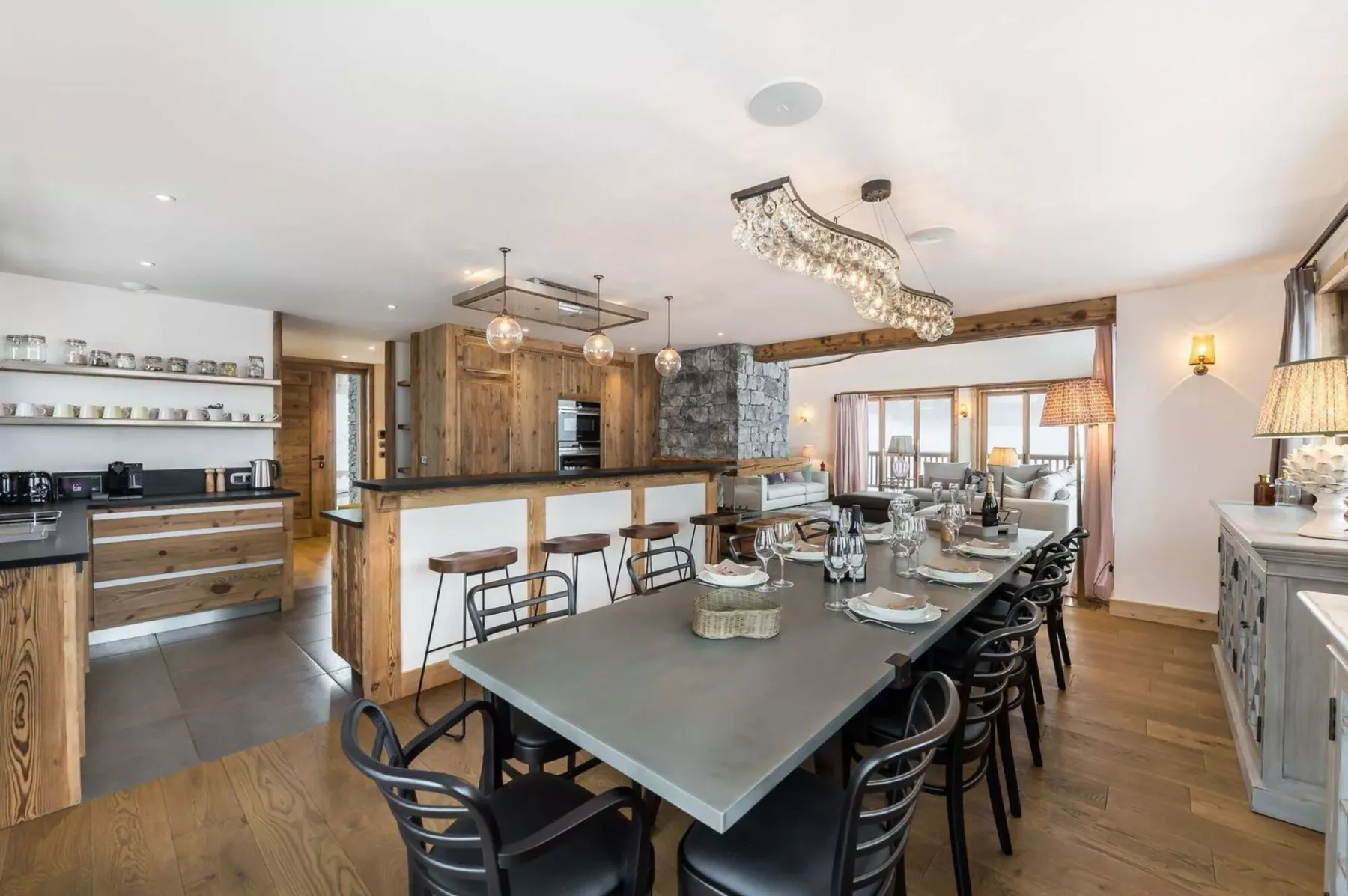 A dining area with a long table and kitchen counters in the background.