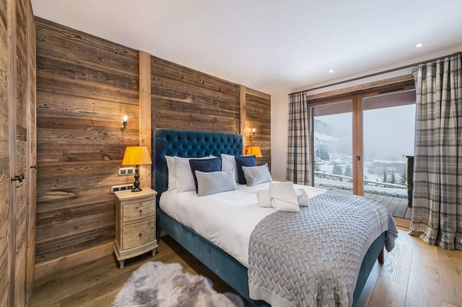 A bedroom with a bed, wood-paneled walls, and large windows overlooking a snowy landscape.