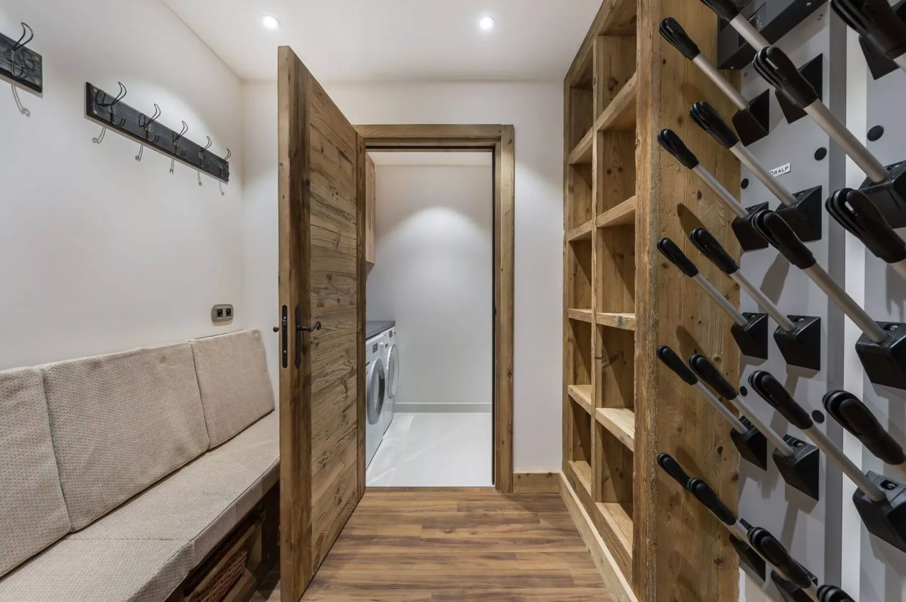 A narrow interior hallway with a bench, open shelving, and a door to a laundry area.