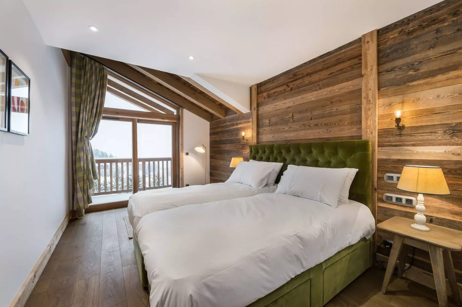 A bedroom with two beds, a green upholstered headboard, and a balcony window.