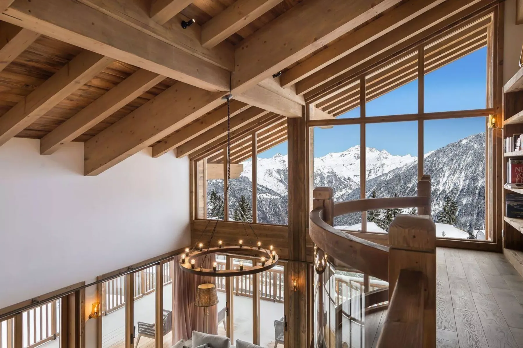 A timber-framed interior overlooks snowy mountains through large windows.