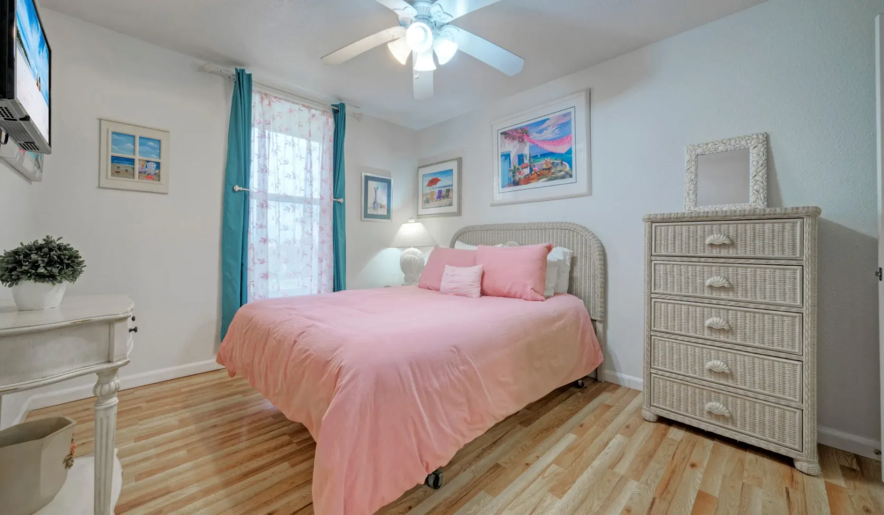 Un dormitorio con una cama rosa, cuadros enmarcados y una cómoda alta.