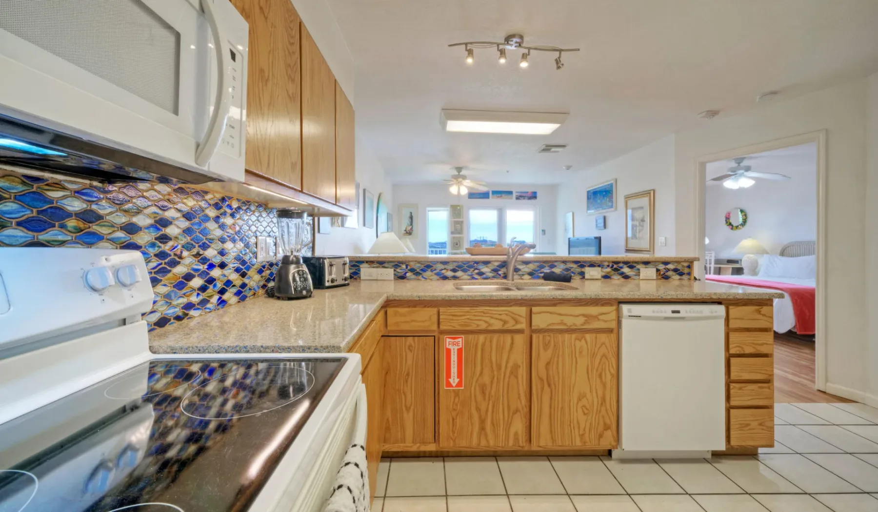 Una cocina con gabinetes de madera y un salpicadero de azulejos se abre a un dormitorio.