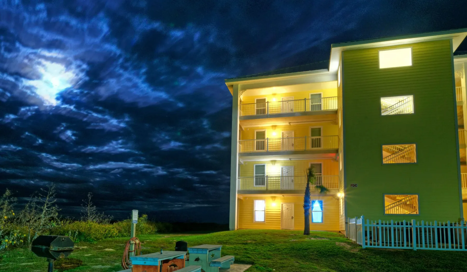 Un edificio iluminado de varios pisos se alza bajo un cielo nocturno nublado.