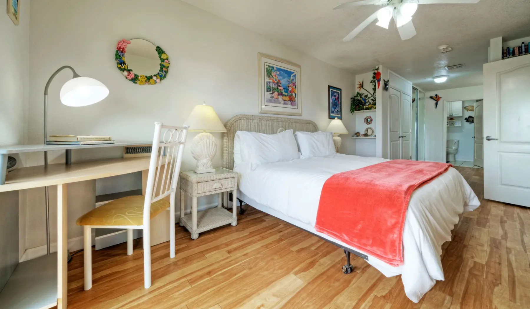 Dormitorio con una cama blanca, un escritorio y una manta coral.