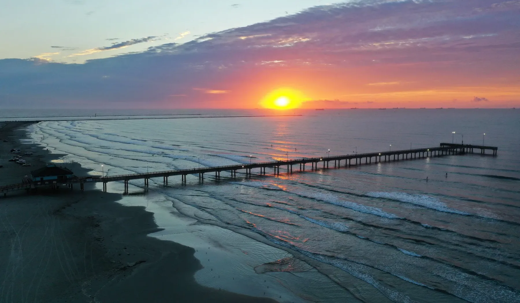 Un atardecer sobre el océano, con un muelle que se extiende sobre las olas.