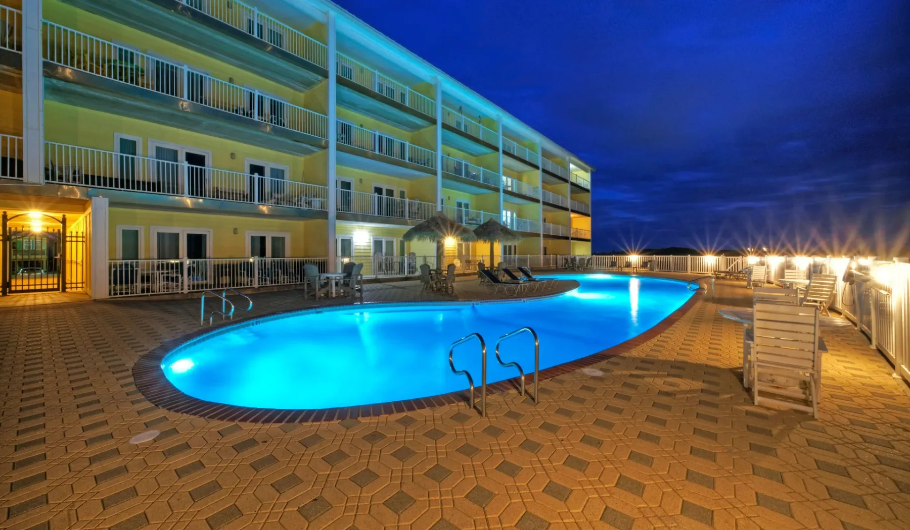 Una piscina exterior iluminada está junto a un edificio de varios pisos por la noche.