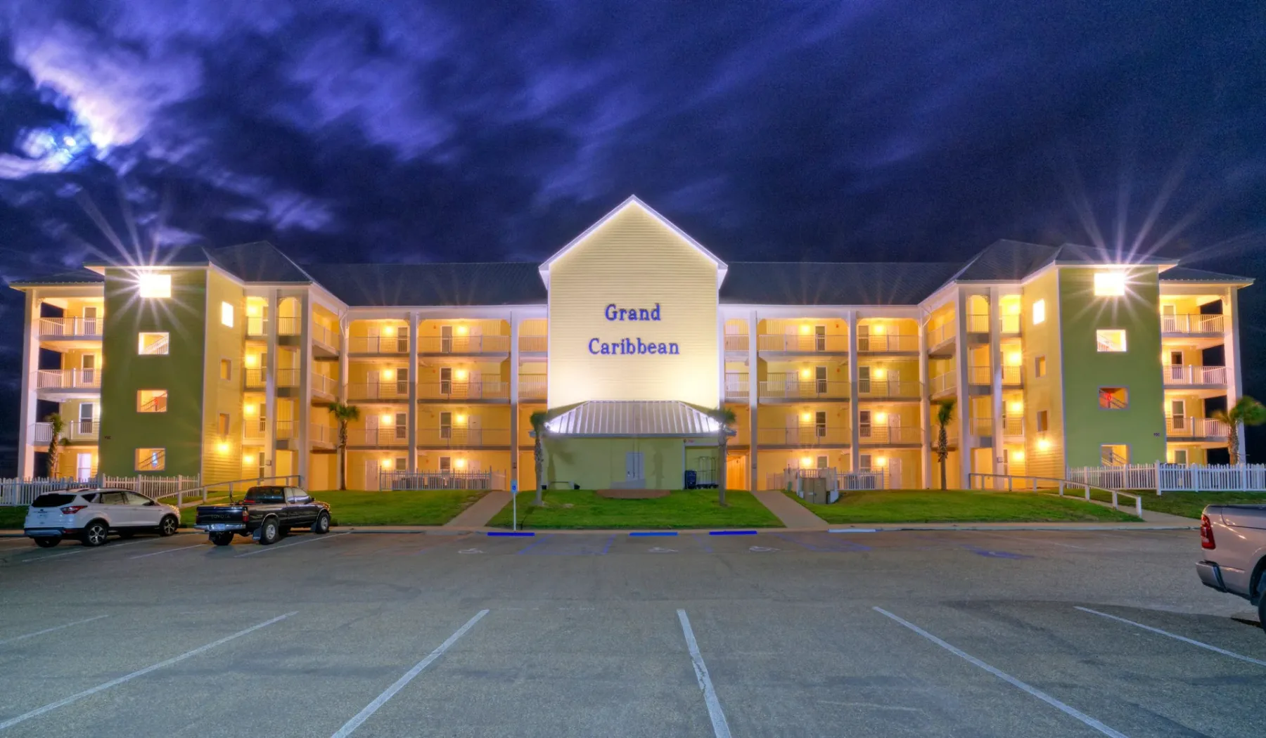 Un edificio hotelero está iluminado por la noche junto a un estacionamiento.