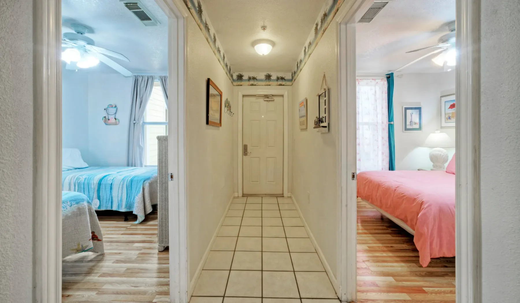 Un pasillo con suelo de baldosas da a dos dormitorios, uno con ropa de cama azul y otro rosa.