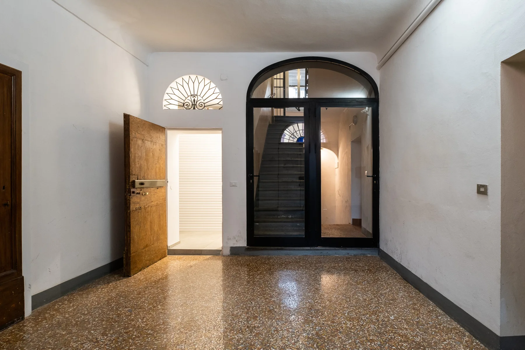 Un recibidor luminoso con una puerta arqueada de marco oscuro y suelo pulido.