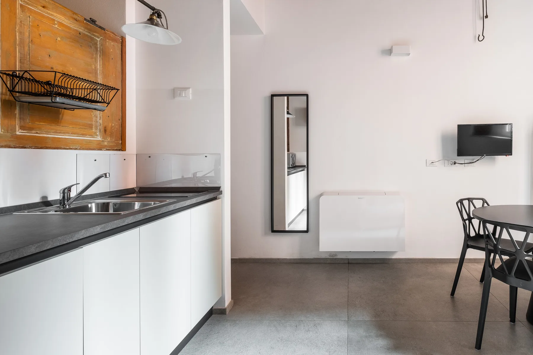 Una cocina compacta con zona de comedor, encimera, mesa y televisor en la pared.