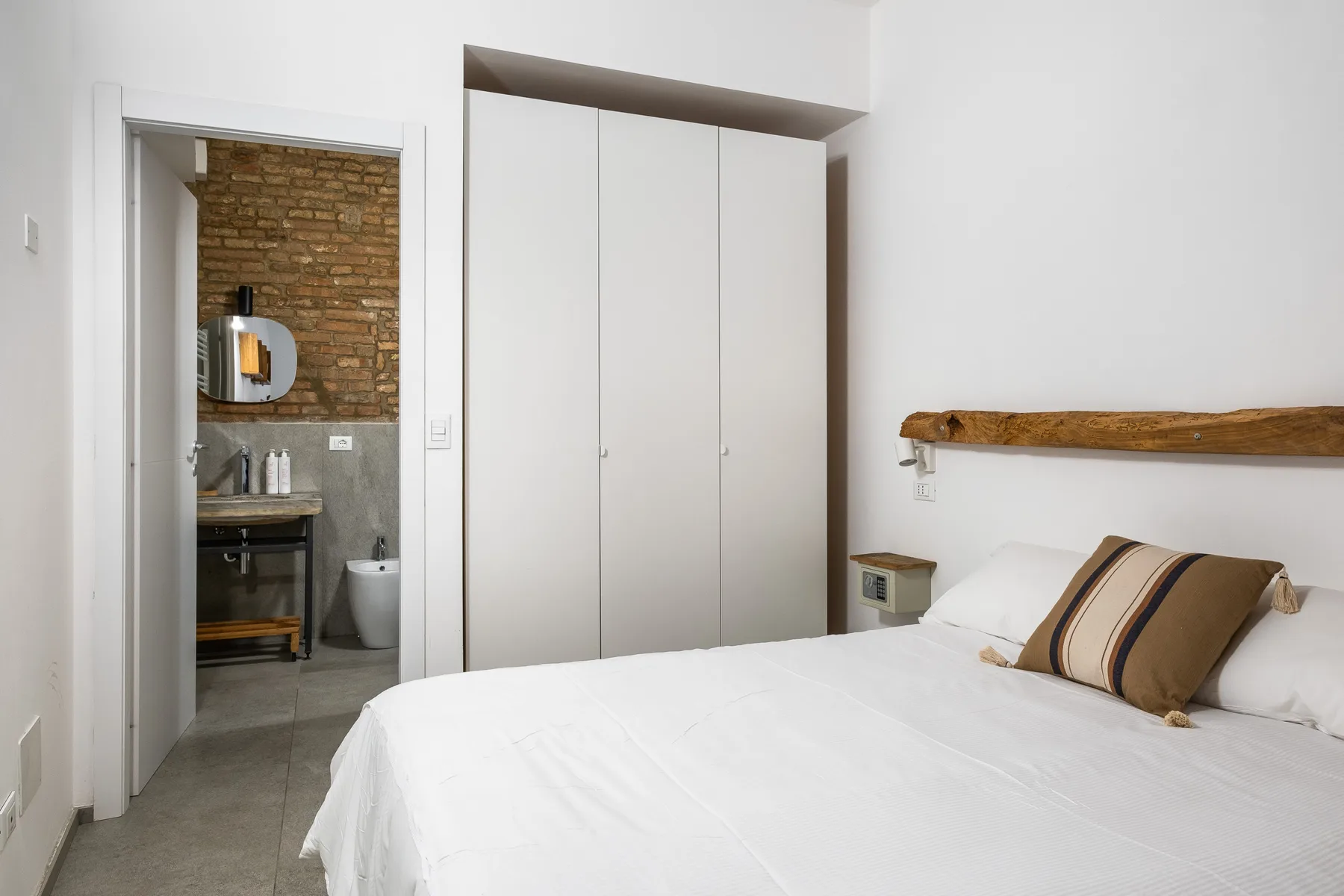 Un dormitorio con una cama blanca, cojines a rayas y un armario empotrado.