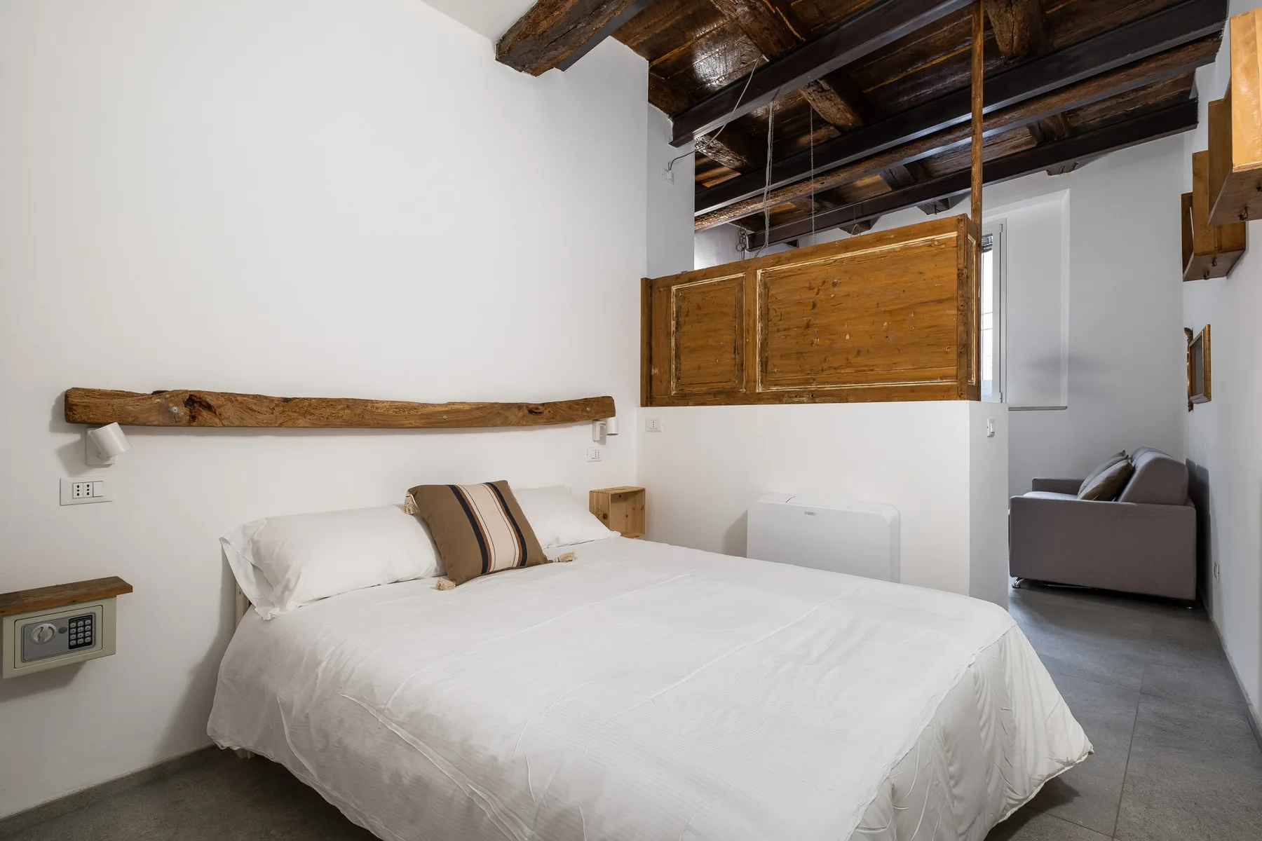 Un dormitorio con una cama bien tendida bajo vigas oscuras a la vista.