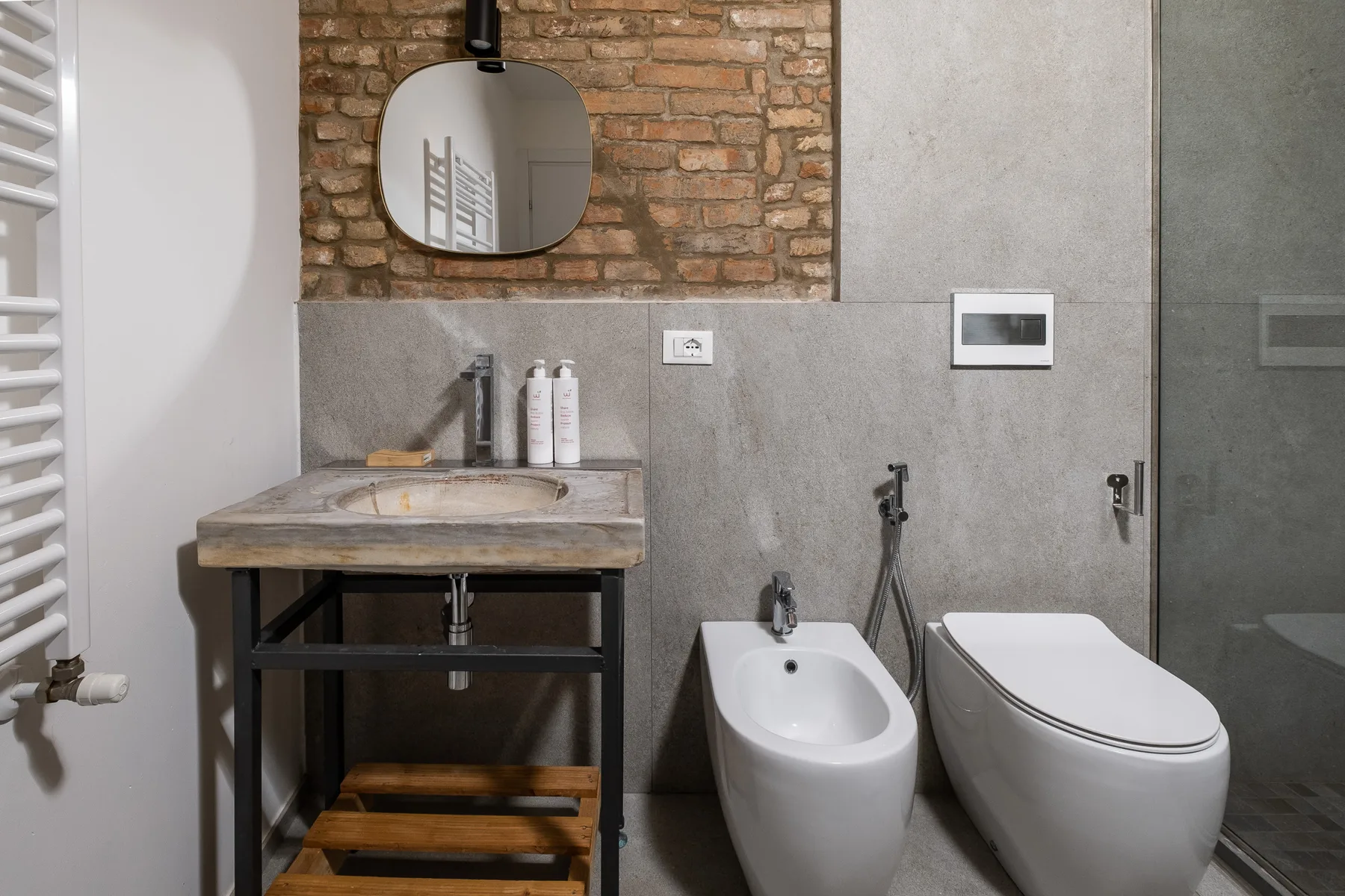 Un baño con lavabo, inodoro y bidé junto a una pared de azulejos grises.