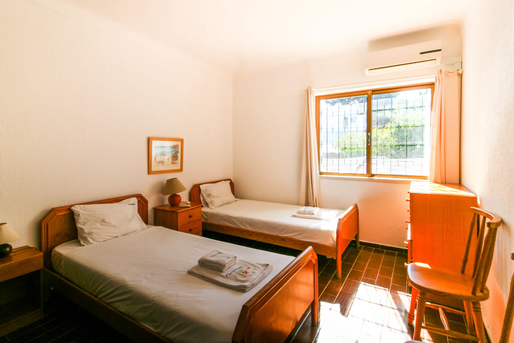 A bright bedroom with two beds beside a sunlit window.
