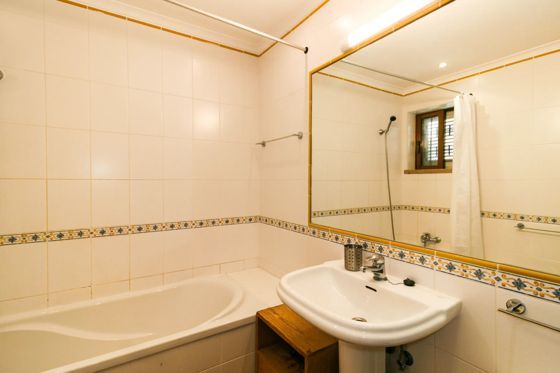 Un baño alicatado con bañera, lavabo y un gran espejo de pared.