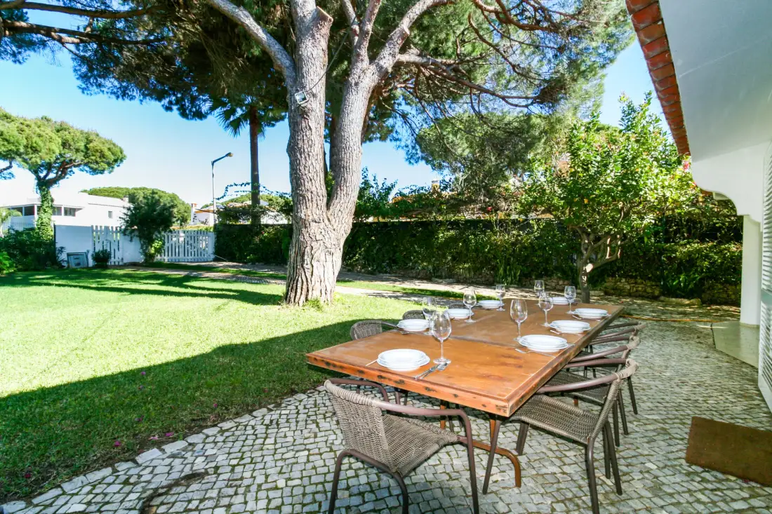 Comedor al aire libre con una mesa de madera junto a un jardín con césped.