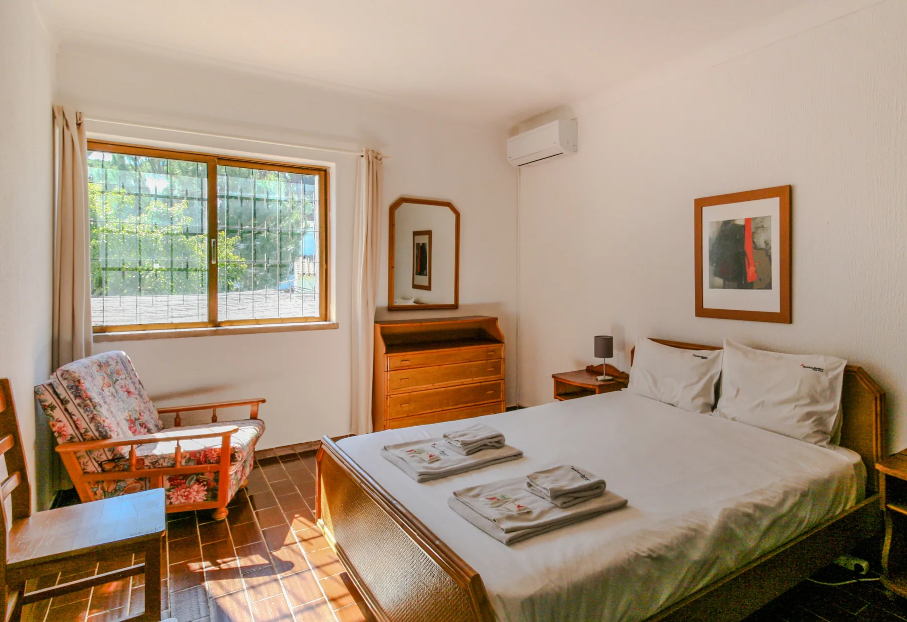 Un dormitorio con una cama grande, una cómoda de madera y una ventana con vistas a la vegetación.