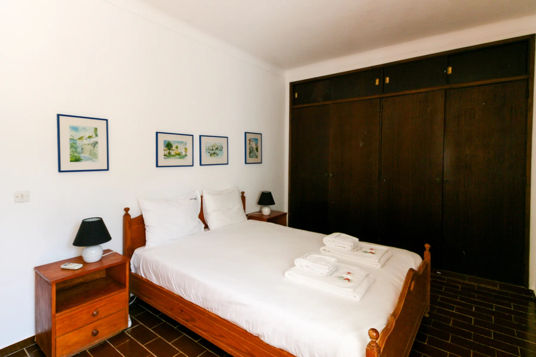 A bedroom with a wooden bed, white bedding, and a dark wardrobe.