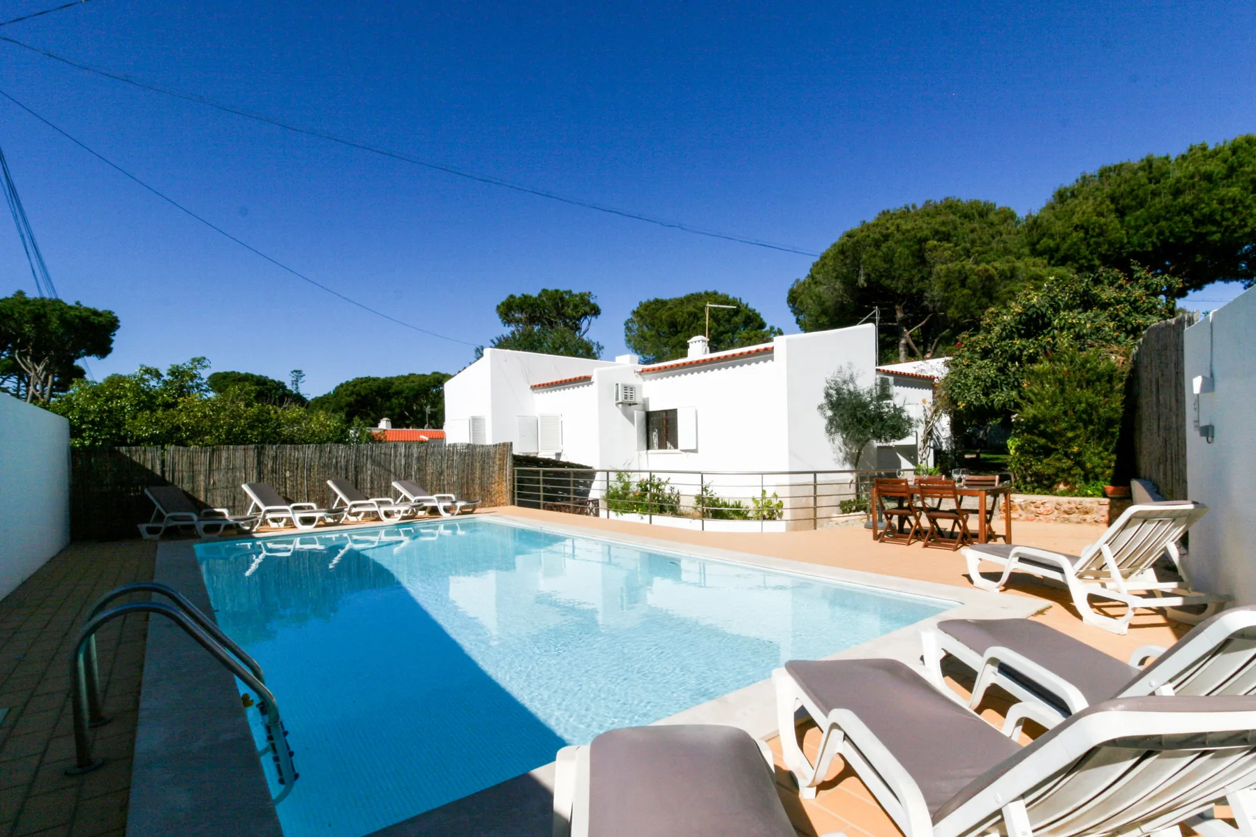 Una piscina junto a una casa blanca, con asientos reclinables alrededor.