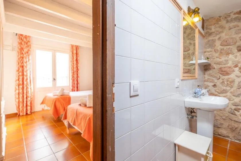 A bathroom with a pedestal sink and a doorway opening to a bedroom.