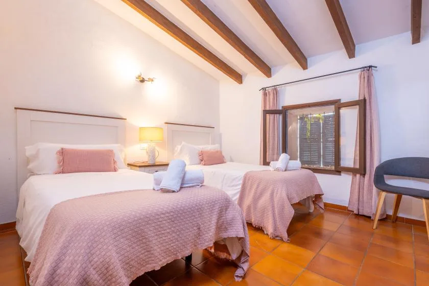 A bedroom with two beds, bedside lighting, and exposed ceiling beams.