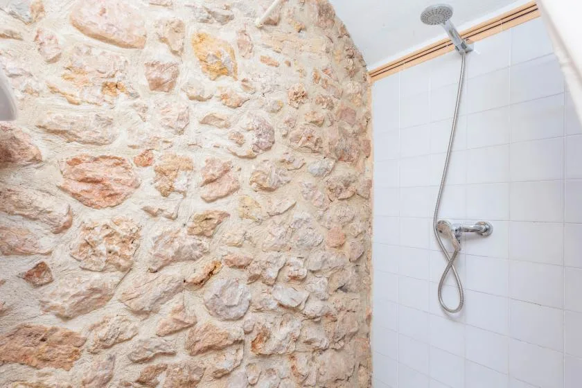 A shower area with a stone wall beside white tiled walls.