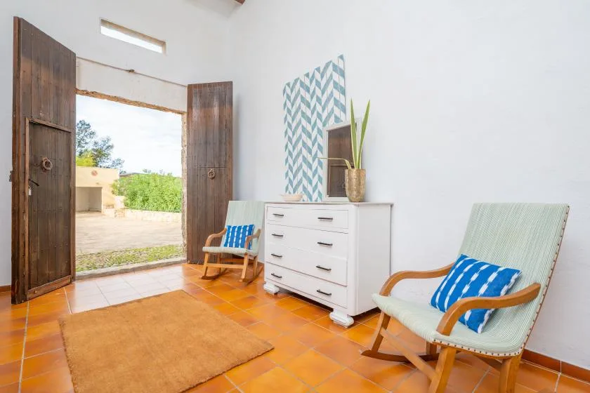A bright sitting room with two cushioned seats and an open doorway.