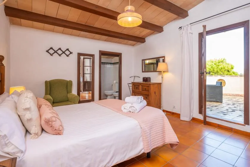 A bedroom with a large bed, green seating, and an open doorway to a patio.