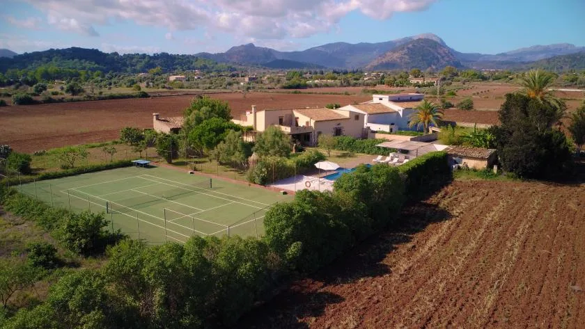 A rural property sits beside a tennis court and swimming pool, with fields and hills beyond.