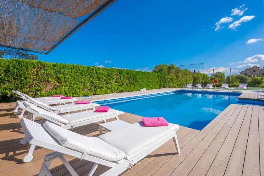 An outdoor swimming pool is bordered by lounge seating on a wooden deck.