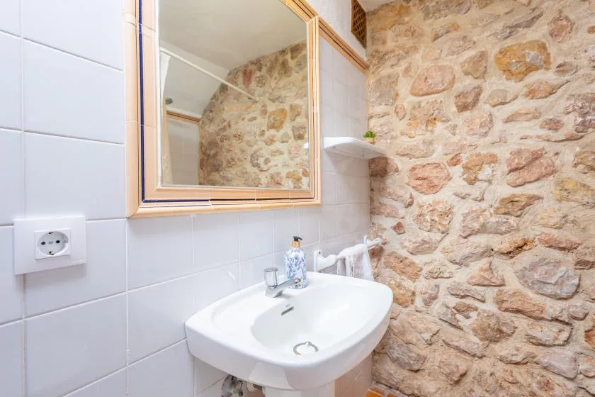 A bathroom sink and mirror sit beside a wall with exposed stone.