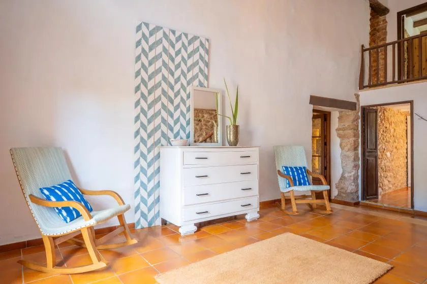 A sitting area with light-colored seating, a dresser, and patterned wall decor.