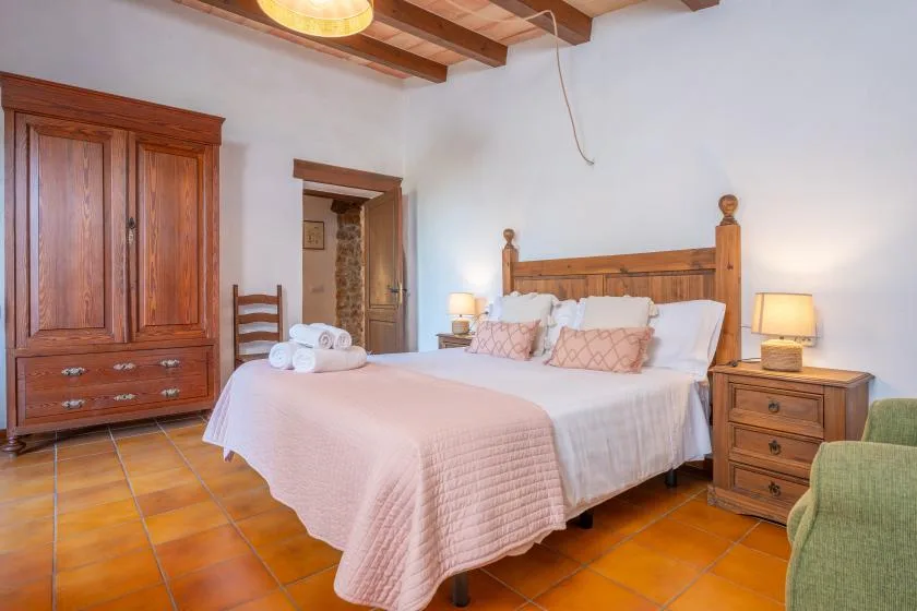 A bedroom with a wooden bed, pale bedding, and terracotta floor tiles.