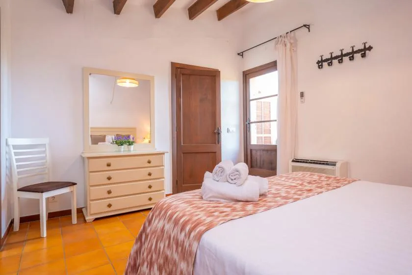 A bedroom with a wooden door, dresser, and bed covered by a patterned blanket.