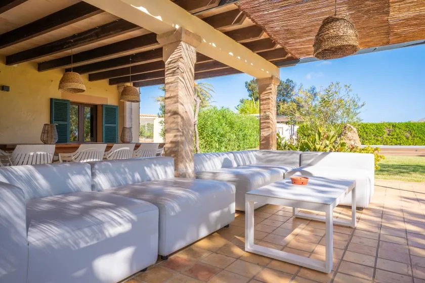 A covered outdoor lounge with white seating and a low table.