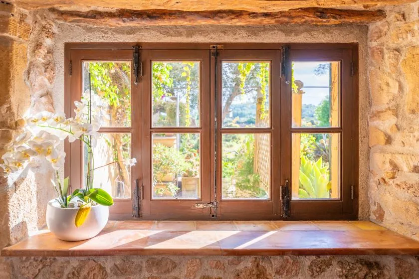 A wooden-framed window set into a stone wall overlooks leafy greenery.