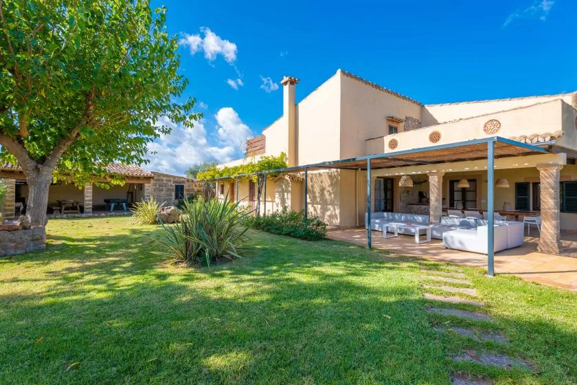 A garden lawn and leafy tree lead to a house with a covered patio.