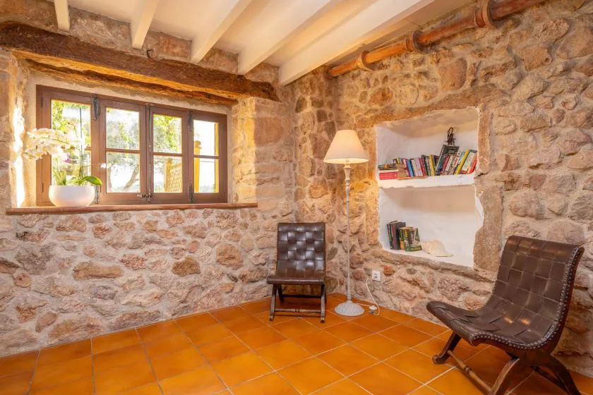 A stone-walled room with a window, built-in shelves, and seating.