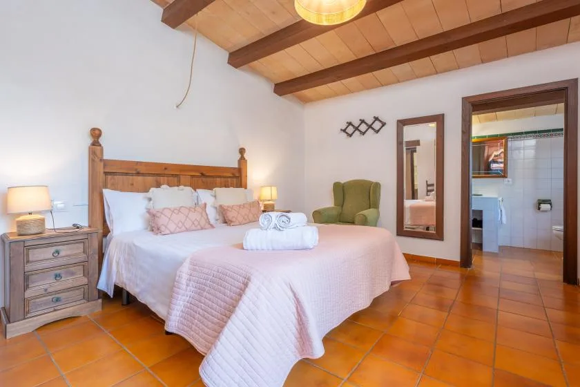 A bedroom with a wooden bed, white bedding, and a green armchair.