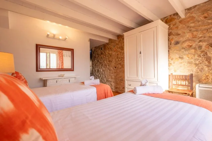 A bedroom with two beds, a white wardrobe, and exposed stone walls.
